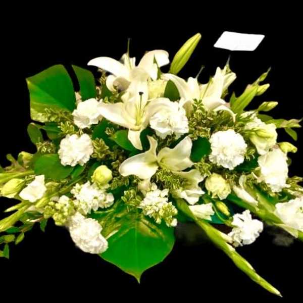White lilies and carnations arranged with broad green leaves