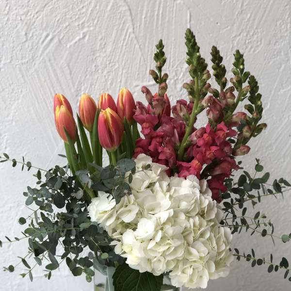 Bouquet of pink tulips, white hydrangeas, and magenta snapdragons in a glass vase