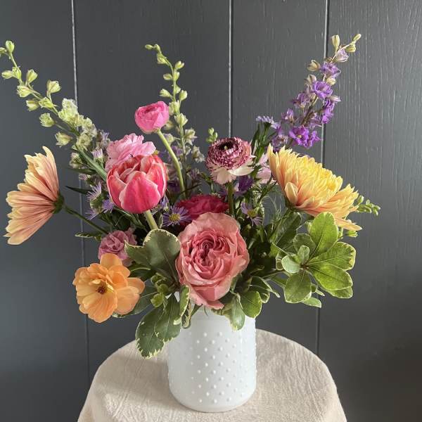 Mixed bouquet of pink, peach, yellow, and purple flowers in a white vase