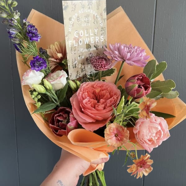 Hand-tied bouquet of pink, purple, and peach flowers wrapped in orange paper