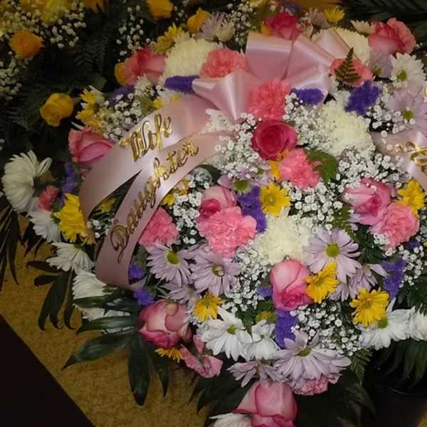 Heart-shaped floral arrangement with pink roses and pastel daisies, tied with ribbons