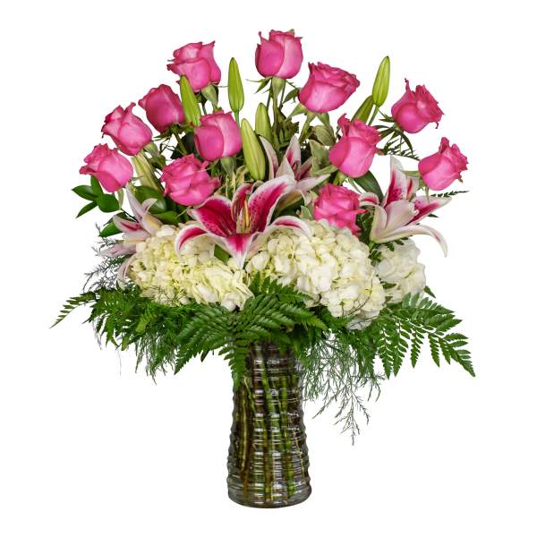 Pink roses and white lilies arranged in a glass vase with white hydrangeas.