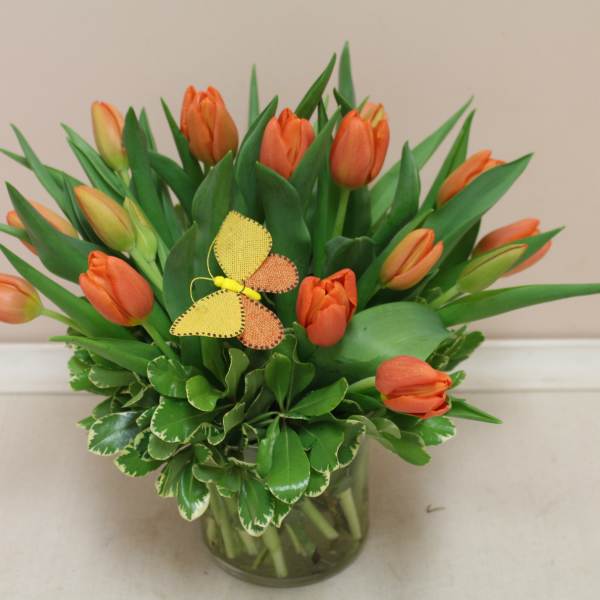 Orange tulips arranged in a glass vase with a small butterfly decoration