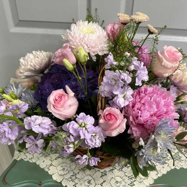 Basket arrangement of pink and lavender flowers with roses and chrysanthemums