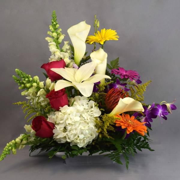 Mixed bouquet with white lilies, red roses, and colorful daisies in a low container
