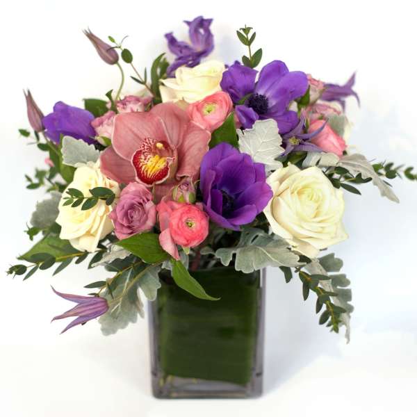 Bouquet of purple, pink, and white flowers in a square glass vase