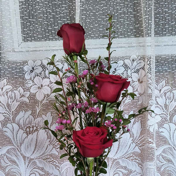 Three red roses in a glass vase with a small white teddy bear