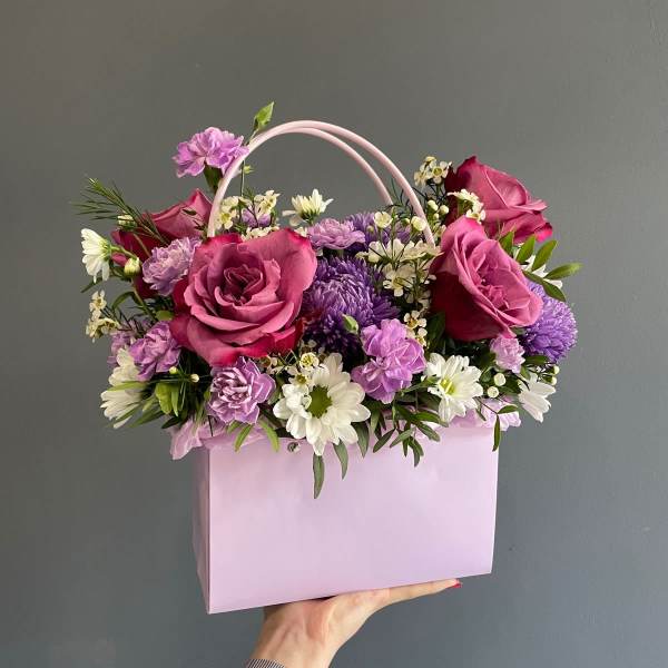 Pink and purple flower arrangement in a pastel gift bag