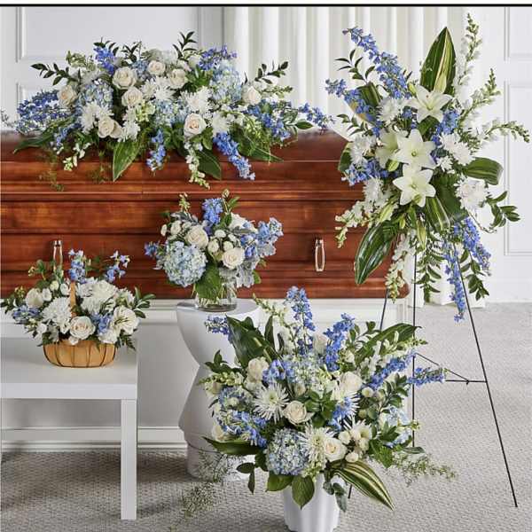 Collection of white and blue funeral flower arrangements around a wooden casket.