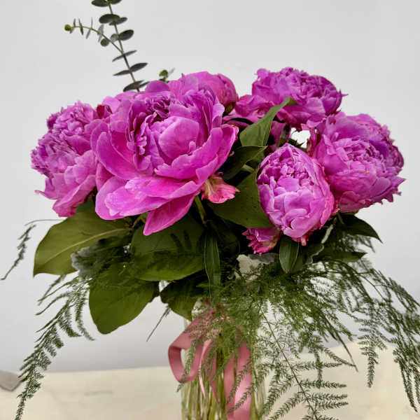 Pink peonies arranged in a clear glass vase with trailing greenery