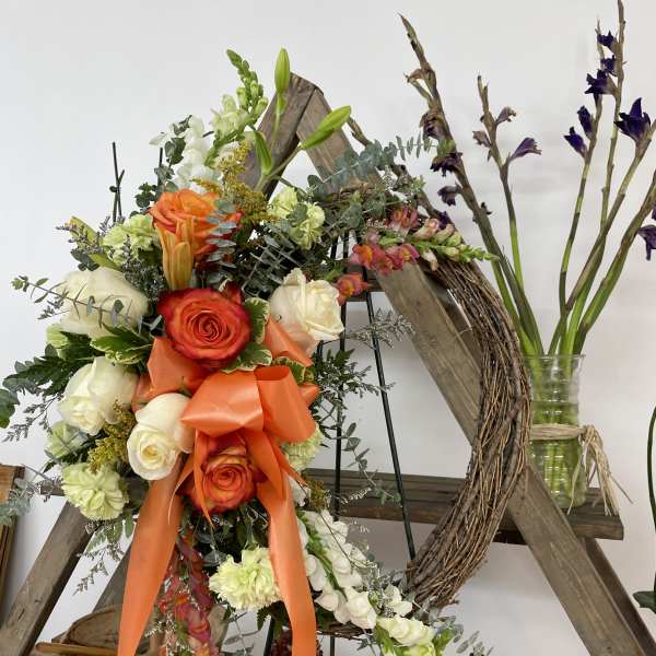 Orange and white floral wreath with roses and lilies on a wooden frame