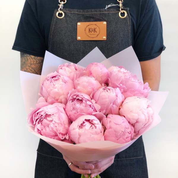 Handheld bouquet of pink peonies wrapped in pale pink paper