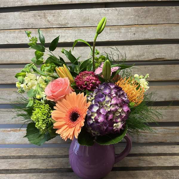 Mixed bouquet in a purple pitcher vase with pink, orange, and purple blooms