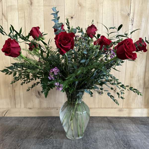 Red roses arranged in a clear glass vase with mixed greenery