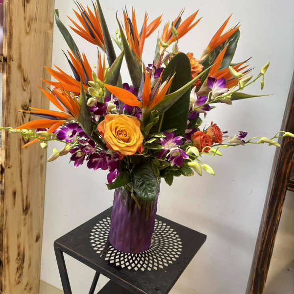 Orange bird of paradise bouquet with purple orchids in a vase