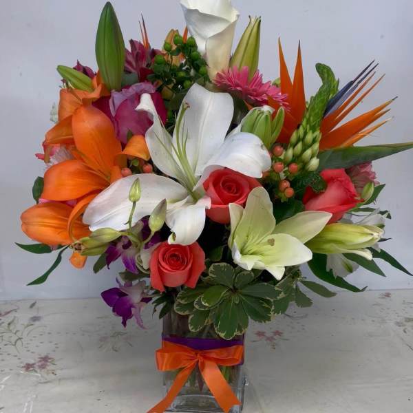 Colorful mixed bouquet in a square glass vase with lilies, roses, and orchids