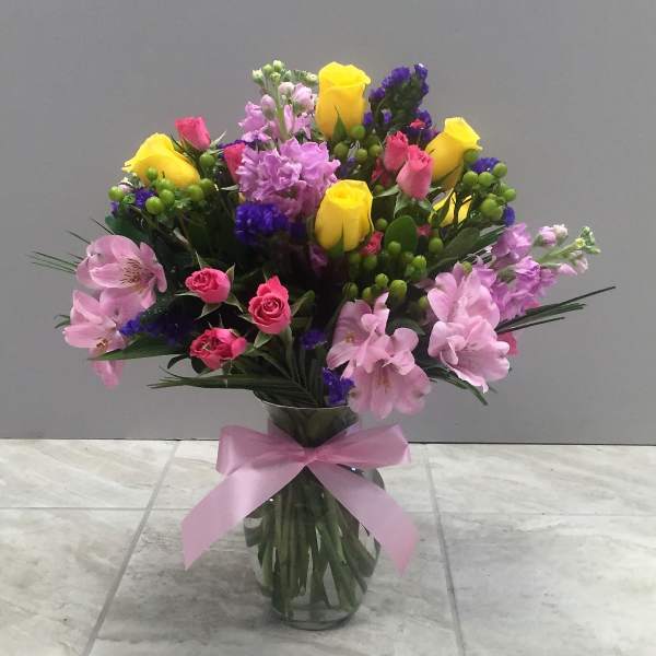 Bouquet of pink, yellow, and purple flowers in a glass vase with a pink ribbon