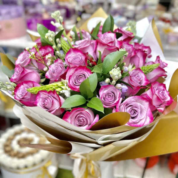 Hand-tied bouquet of pink roses with white accent flowers in cream and gold wrapping