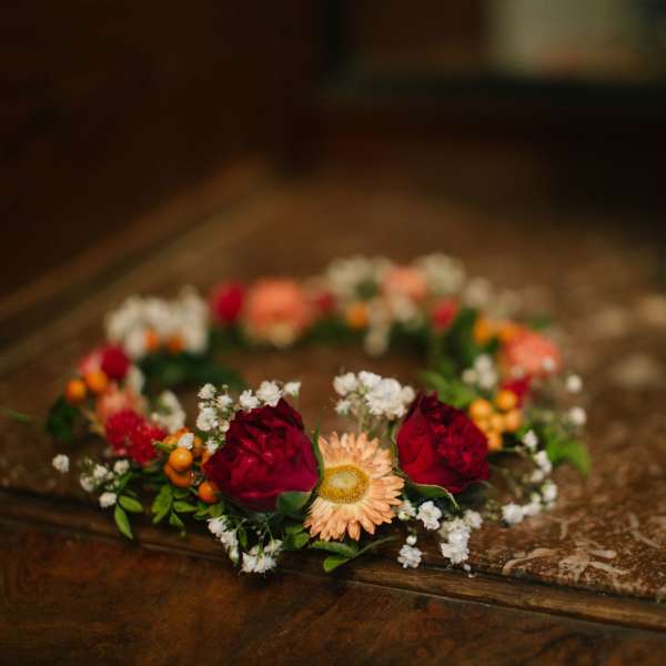 Floral crown with red roses and peach daisies on a table
