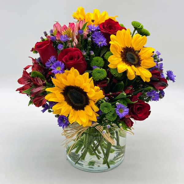 Bouquet of sunflowers, red roses, and purple flowers in a glass vase