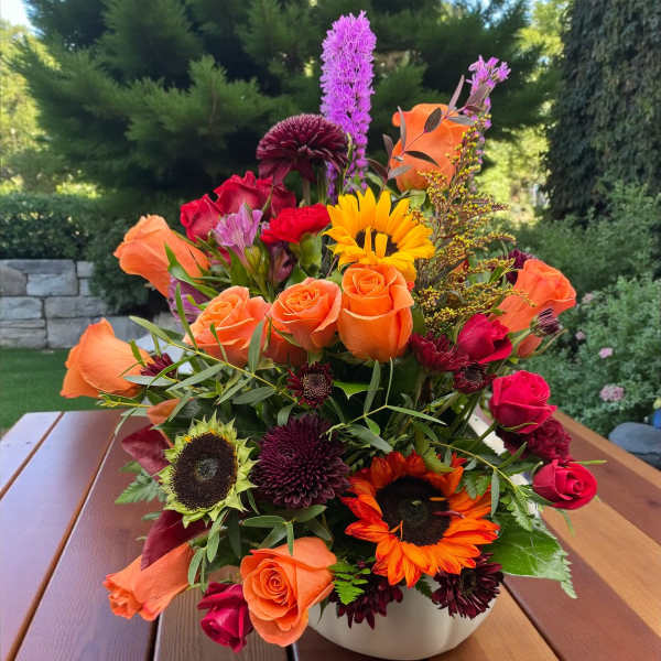 Mixed bouquet of orange and red flowers in a white bowl vase