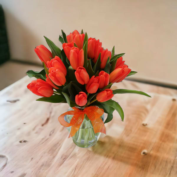 Bouquet of orange tulips in a clear glass vase with an orange ribbon