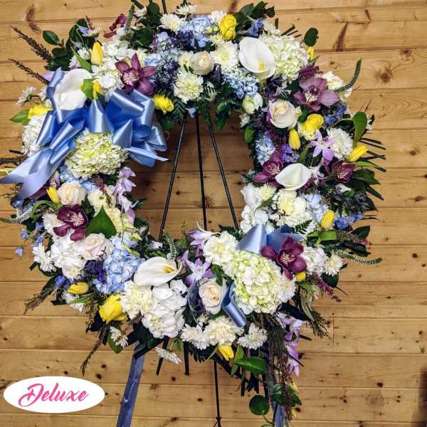 Large floral wreath with mixed blooms and blue ribbon on a stand