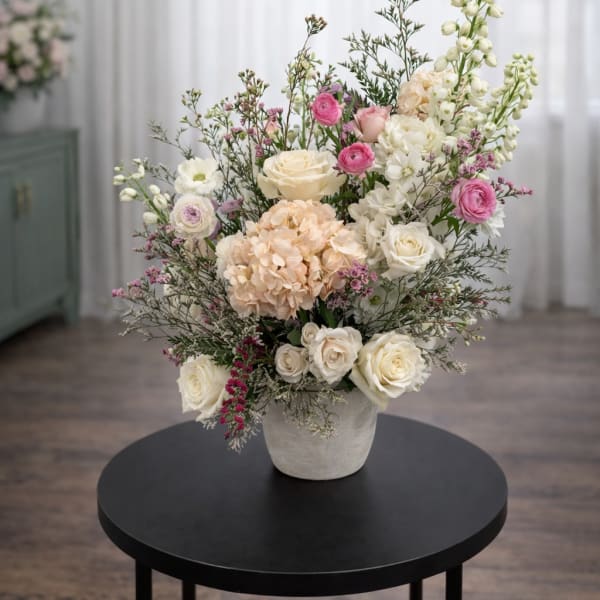 Tall floral arrangement in a gray vase with white, pink, and peach blooms