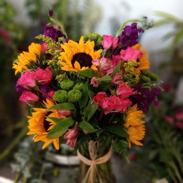 Mixed bouquet with sunflowers, pink roses, and purple flowers in a glass vase