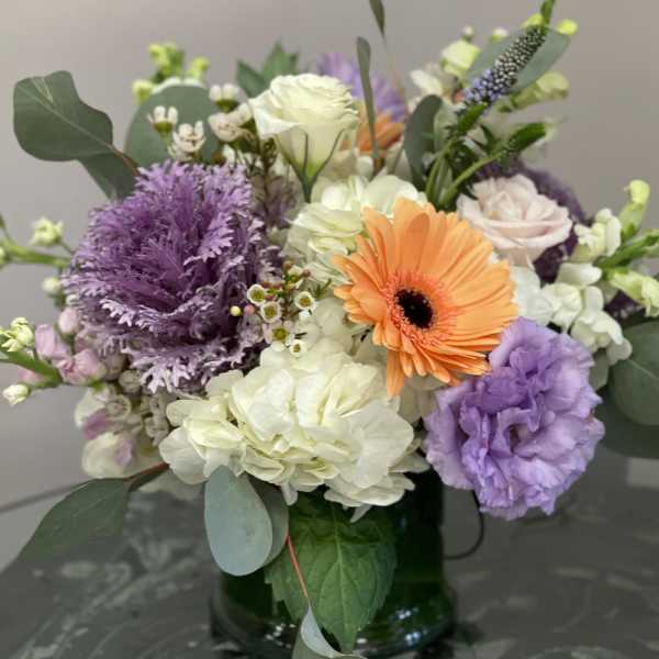 Mixed bouquet with orange gerbera daisies, white roses, and purple blooms in a glass vase