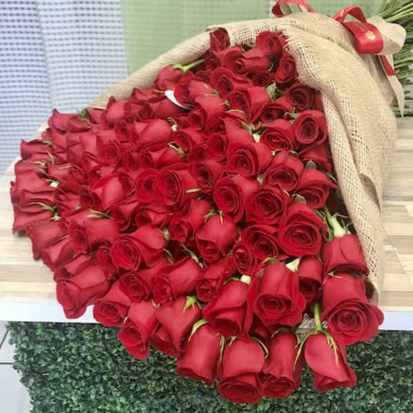 Large bouquet of many red roses wrapped in burlap with a red ribbon bow.