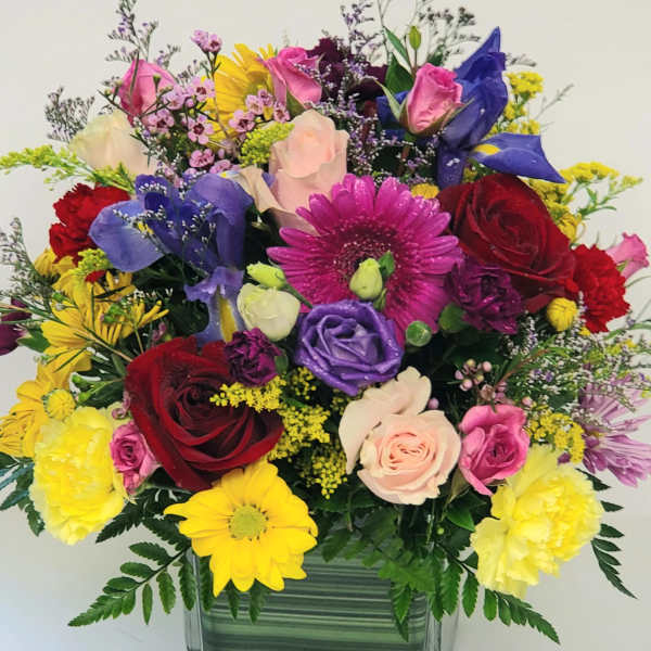 Mixed bouquet in a square glass vase with roses, daisies, and colorful blooms