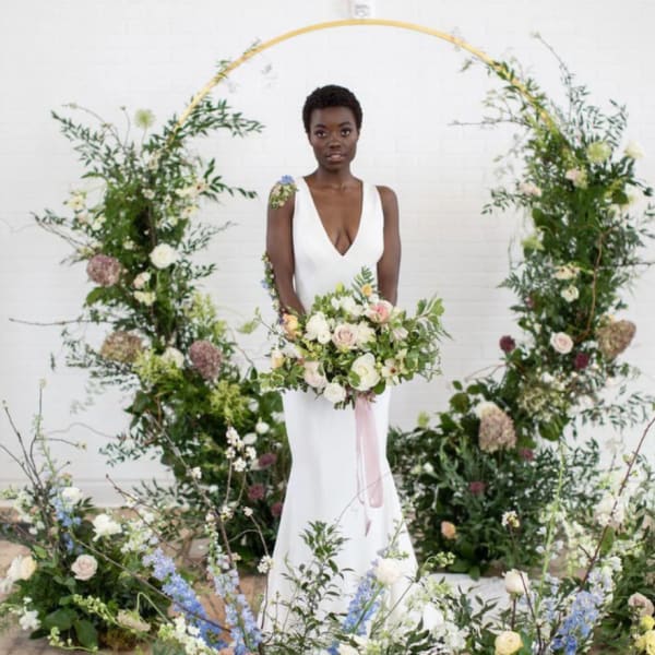 Bride holding a bouquet in front of a floral arch