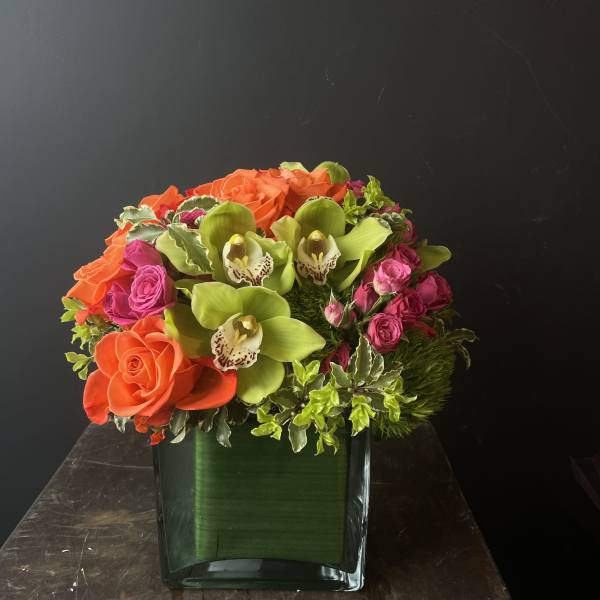 Orange roses and green orchids in a square glass vase