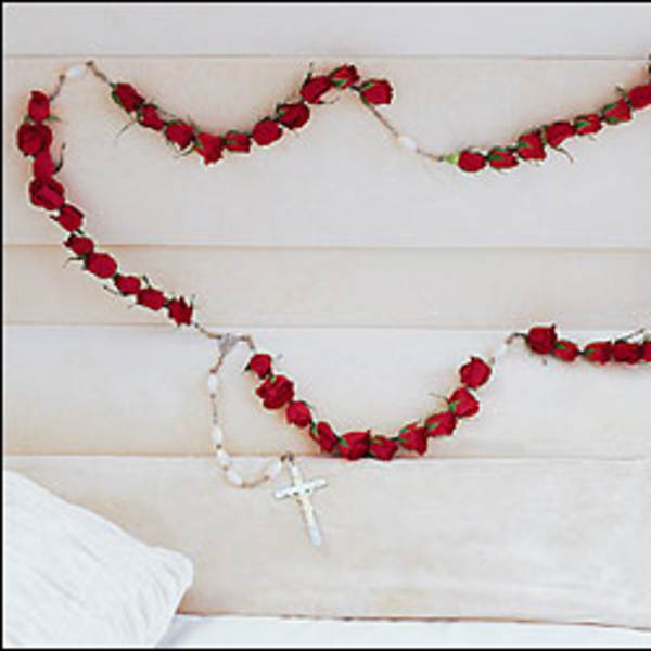 Red rose garland draped on a white upholstered headboard with a rosary cross