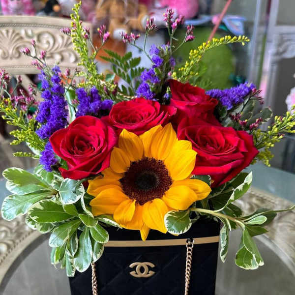 Red roses and a sunflower in a black gift bag arrangement