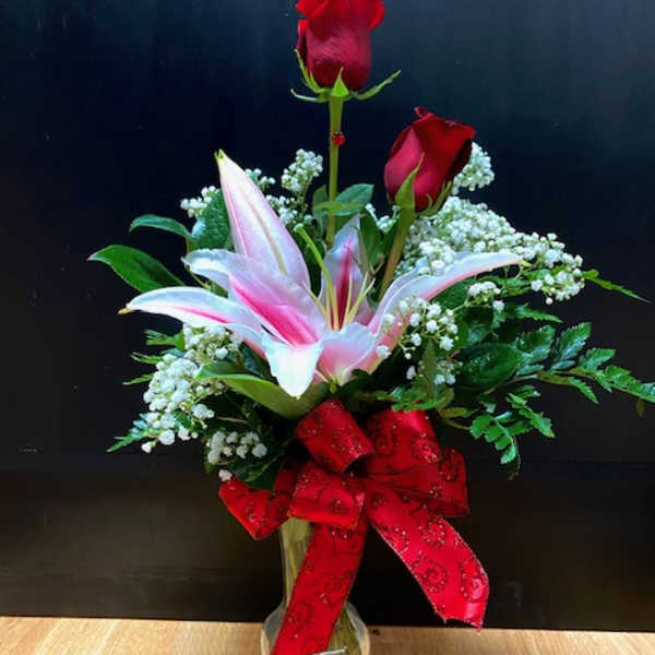 Red roses and pink lilies in a clear glass vase with a red bow