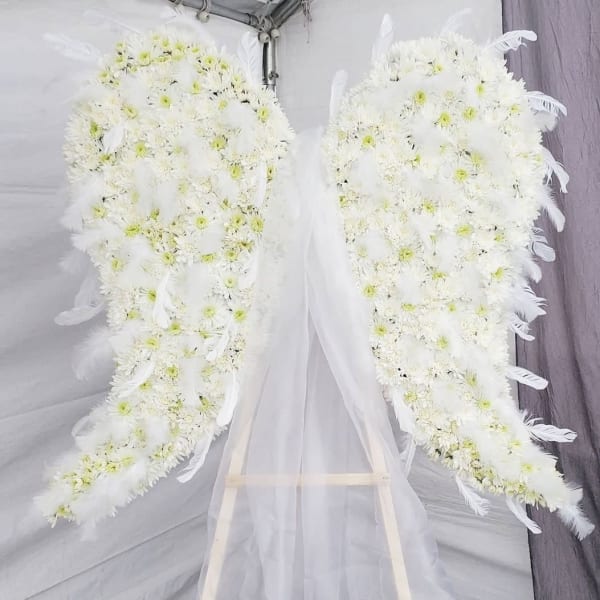Two white floral funeral sprays with feather accents on an easel