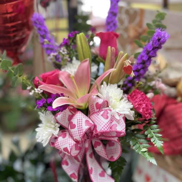 Pink lilies and roses with white daisies and a heart-patterned ribbon in a vase
