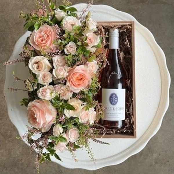 Pink and white rose arrangement beside a wine bottle in a gift box