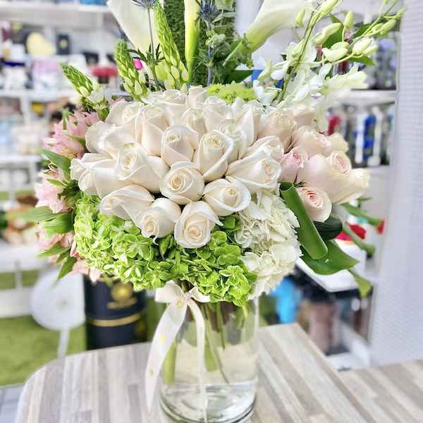 Tall arrangement of white roses, calla lilies and green hydrangeas in a clear glass vase