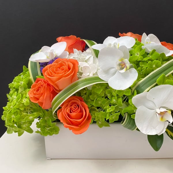 Orange roses and white orchids arranged in a white rectangular box
