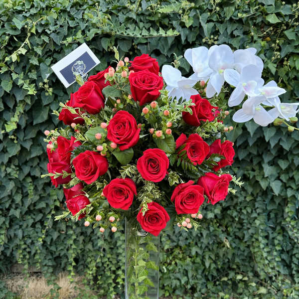 Tall bouquet of red roses with white orchids in a clear vase
