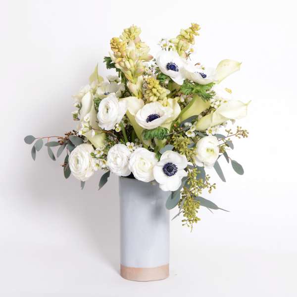 White floral arrangement in a tall gray vase with pale green accents