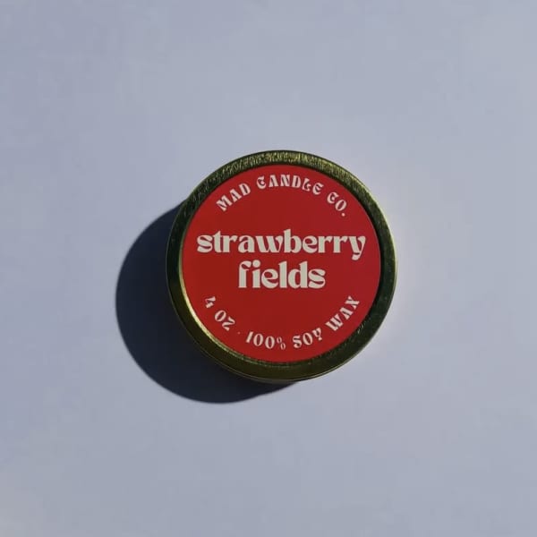 Round red candle tin labeled strawberry fields
