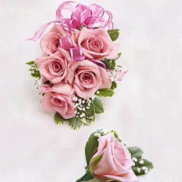 Corsage and boutonniere set with pink roses, white filler flowers, and a pink ribbon bow.