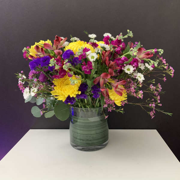 Mixed bouquet of yellow, pink, purple, and white flowers in a glass vase