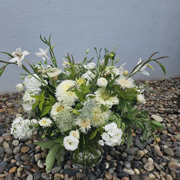 Clear glass vase filled with lush white and cream flowers and abundant leafy accents
