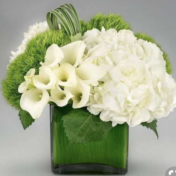 White calla lilies and hydrangeas in a green glass vase