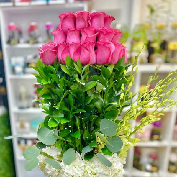 Tall arrangement of pink roses, layered greenery, and white hydrangeas in a pink hatbox.